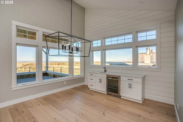 bar with white cabinetry, a towering ceiling, wine cooler, and light wood-type flooring