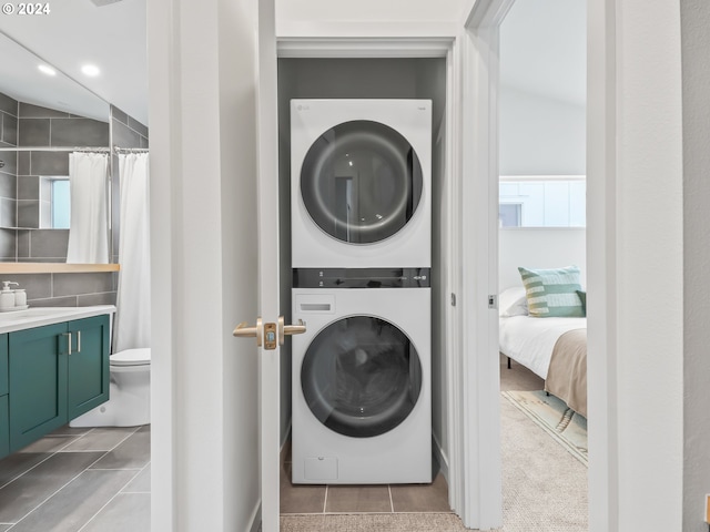 clothes washing area featuring stacked washing maching and dryer, sink, light tile patterned floors, and tile walls