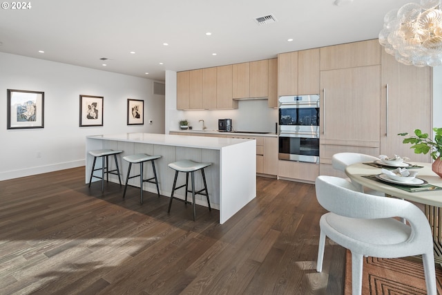 kitchen with visible vents, a kitchen island, light brown cabinetry, double oven, and a kitchen bar