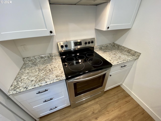 kitchen with white cabinets, light hardwood / wood-style floors, light stone countertops, and stainless steel electric range