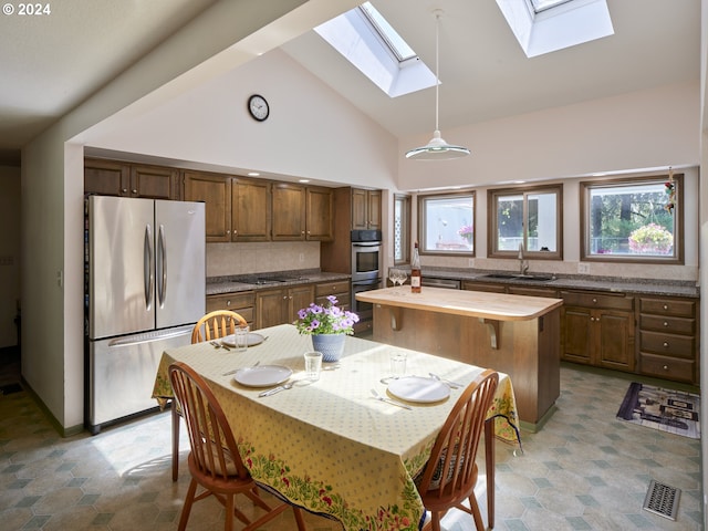 kitchen featuring stainless steel appliances, sink, tasteful backsplash, decorative light fixtures, and high vaulted ceiling