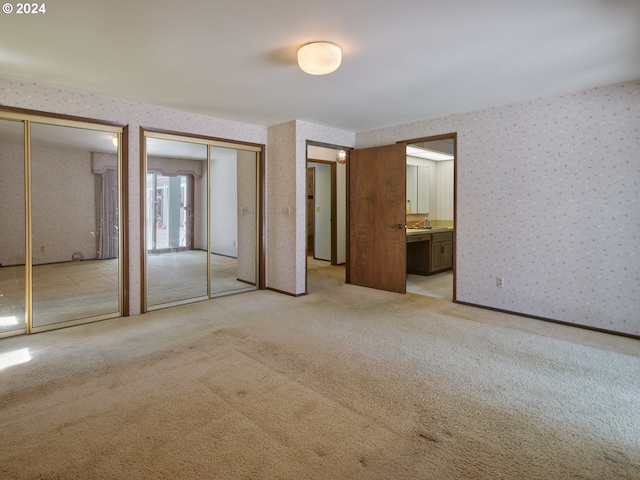 unfurnished bedroom featuring multiple closets, ensuite bath, sink, and light colored carpet