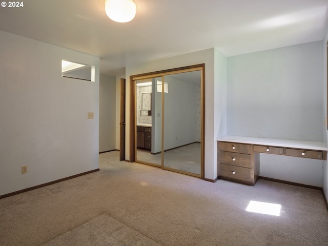 unfurnished bedroom featuring ensuite bathroom, light carpet, and built in desk