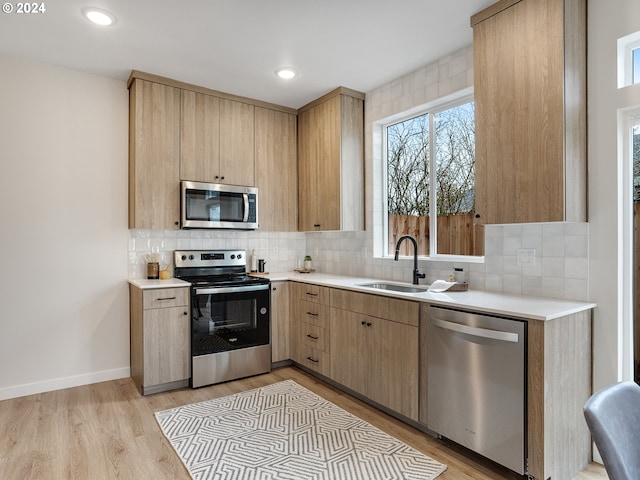 kitchen with appliances with stainless steel finishes, backsplash, sink, and light hardwood / wood-style flooring