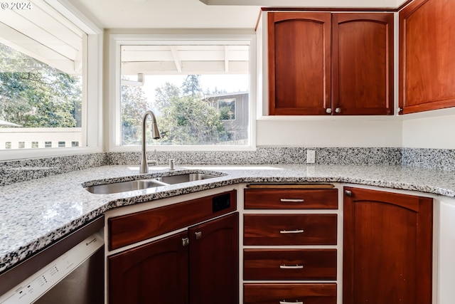 kitchen with a healthy amount of sunlight, dishwasher, a sink, and light stone countertops