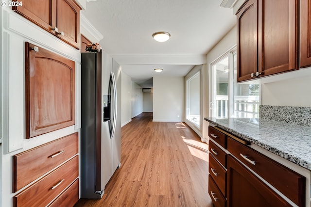 kitchen featuring light stone counters, stainless steel fridge, light wood-style flooring, and baseboards