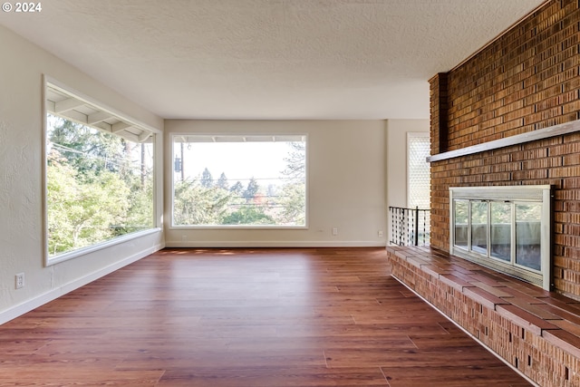 unfurnished living room featuring a textured ceiling, a fireplace, wood finished floors, and baseboards