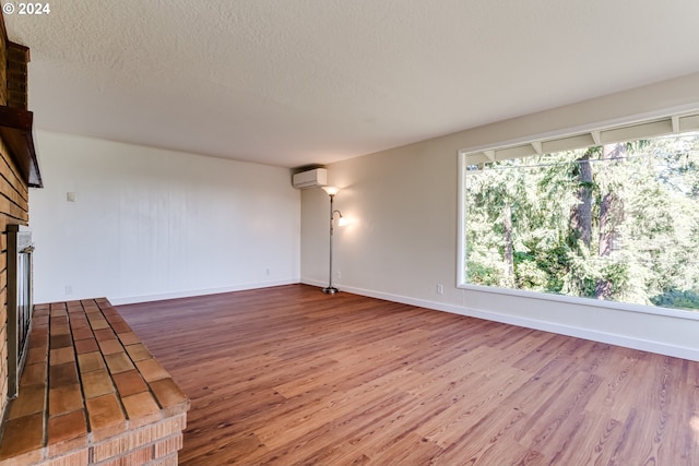 empty room featuring a brick fireplace, a textured ceiling, an AC wall unit, and wood finished floors