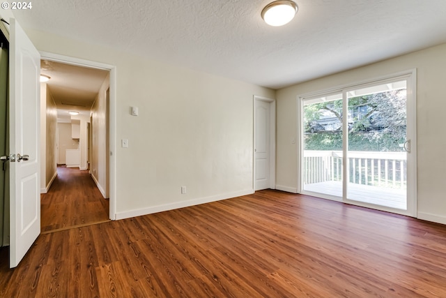 unfurnished room with a textured ceiling, baseboards, and wood finished floors