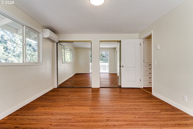 unfurnished room featuring light wood-style floors, an AC wall unit, and baseboards