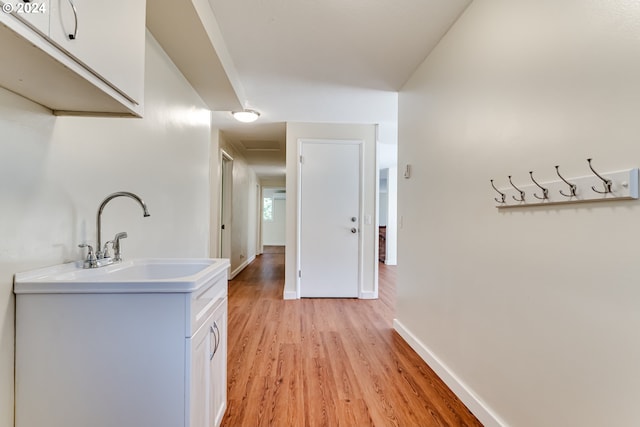 hallway with light wood-type flooring, baseboards, and a sink