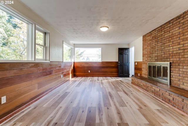 interior space featuring wooden walls, a wainscoted wall, wood finished floors, a textured ceiling, and a brick fireplace