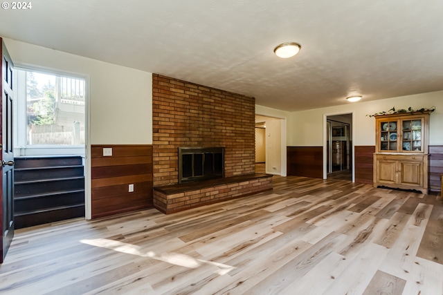 unfurnished living room with a wainscoted wall, wooden walls, a brick fireplace, and light wood-style floors