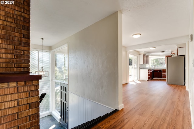 hallway featuring a textured wall, light wood finished floors, and a notable chandelier