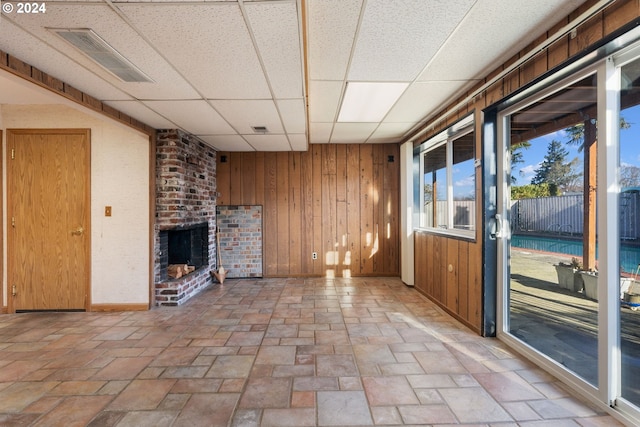 unfurnished living room featuring a fireplace, a drop ceiling, and wood walls