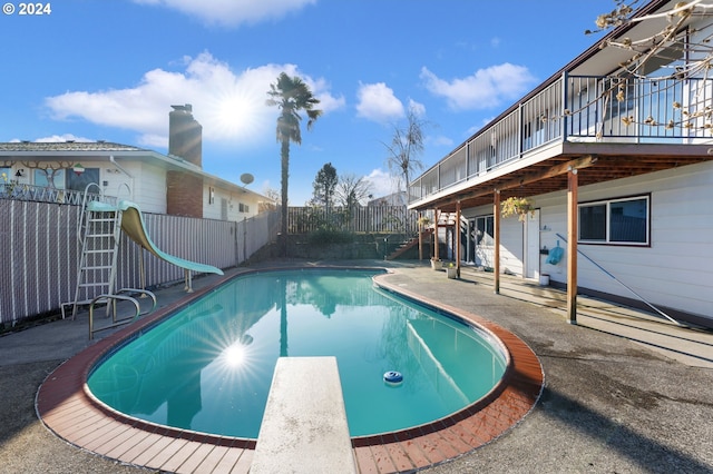 view of swimming pool featuring a diving board, a patio area, a wooden deck, and a water slide