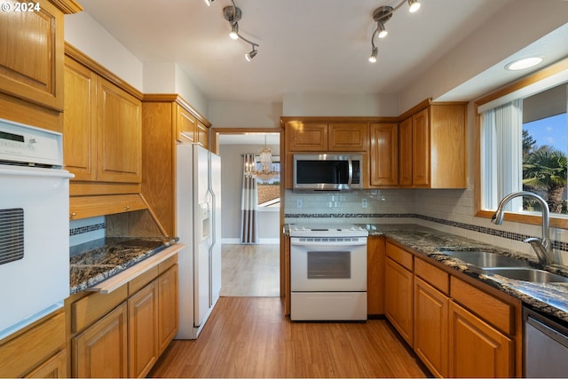 kitchen with backsplash, dark stone counters, stainless steel appliances, sink, and light hardwood / wood-style flooring