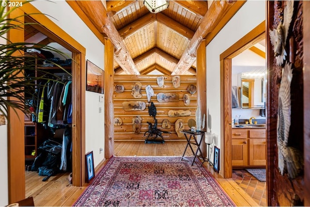 hallway with rustic walls, light wood-type flooring, wooden ceiling, and lofted ceiling with beams