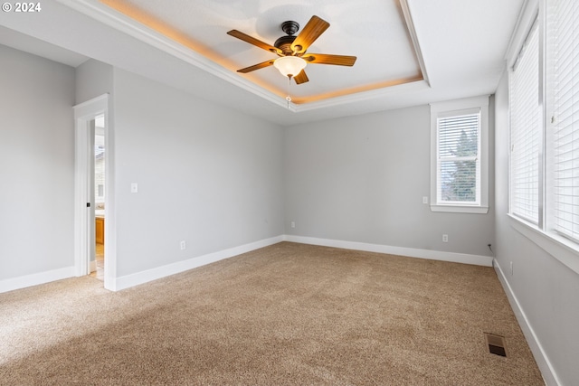 carpeted empty room with a raised ceiling and ceiling fan