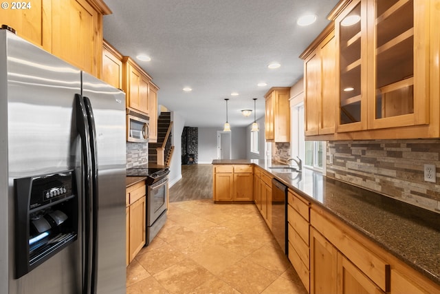 kitchen featuring sink, dark stone countertops, light hardwood / wood-style floors, decorative light fixtures, and appliances with stainless steel finishes