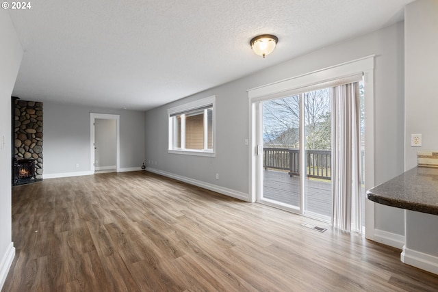 unfurnished living room with hardwood / wood-style flooring, a stone fireplace, and a textured ceiling