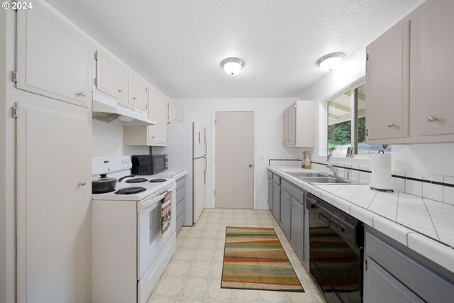 kitchen with gray cabinets, tile countertops, a textured ceiling, black appliances, and sink