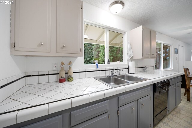 kitchen featuring gray cabinetry, dishwasher, sink, and tile countertops