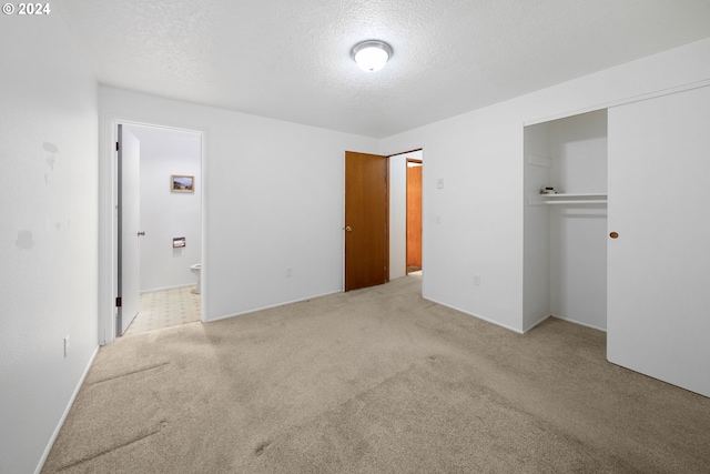 unfurnished bedroom with a textured ceiling, light carpet, ensuite bathroom, and a closet