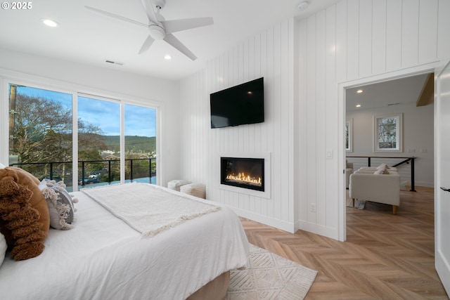 bedroom featuring ceiling fan, light parquet flooring, access to exterior, a large fireplace, and wooden walls