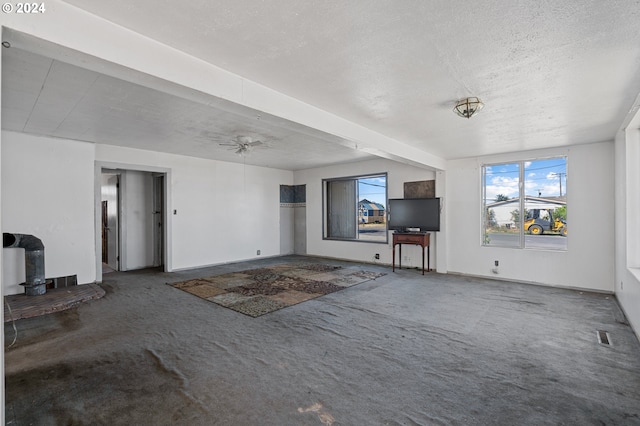 unfurnished living room with a wood stove, ceiling fan, carpet floors, and a textured ceiling