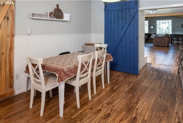 dining area featuring wooden walls, dark hardwood / wood-style floors, and a barn door