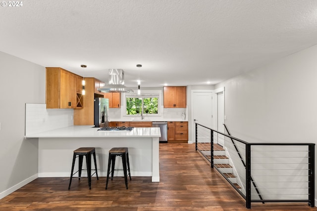 kitchen with appliances with stainless steel finishes, dark hardwood / wood-style floors, kitchen peninsula, a kitchen bar, and island range hood