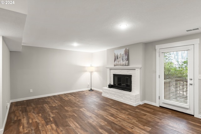 unfurnished living room featuring dark hardwood / wood-style flooring, a textured ceiling, and a brick fireplace