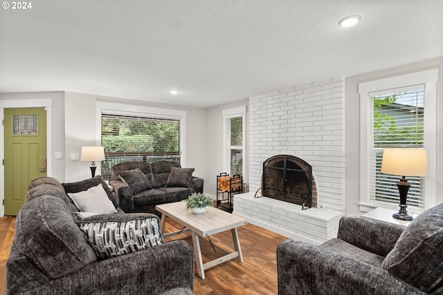 living room with hardwood / wood-style flooring, a textured ceiling, and a brick fireplace