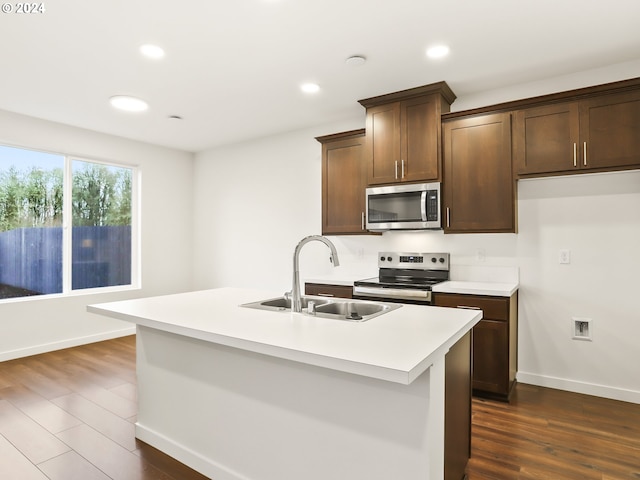 kitchen with a kitchen island with sink, sink, appliances with stainless steel finishes, dark hardwood / wood-style flooring, and dark brown cabinetry