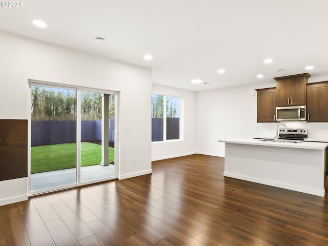 kitchen with sink, stainless steel appliances, dark hardwood / wood-style floors, and a center island with sink