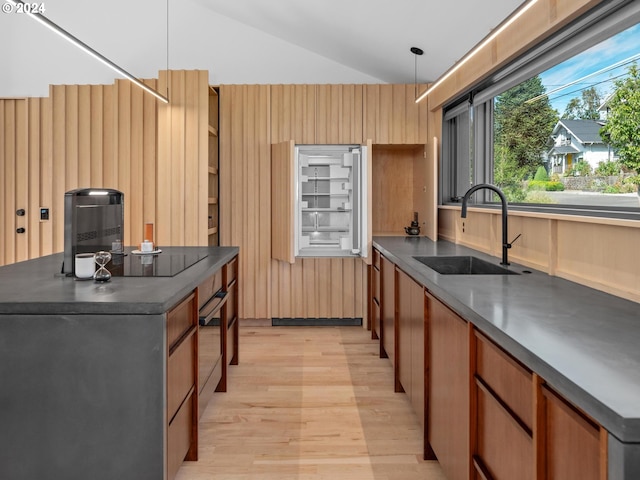 kitchen featuring decorative light fixtures, sink, lofted ceiling, and light hardwood / wood-style floors