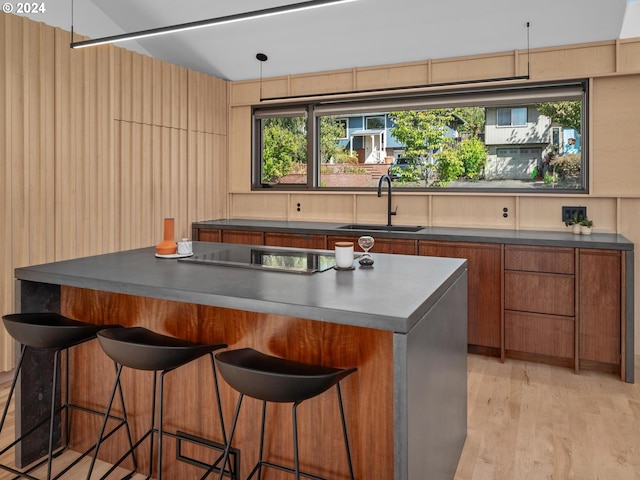 interior space with a breakfast bar area, light wood-type flooring, black stovetop, a center island, and sink