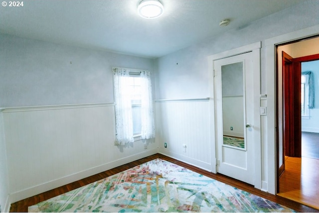 unfurnished bedroom with a wainscoted wall and dark wood-style flooring