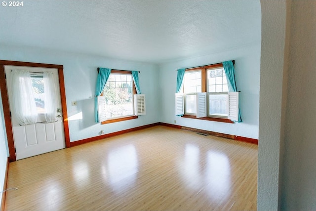 empty room featuring visible vents, a textured ceiling, baseboards, and wood finished floors