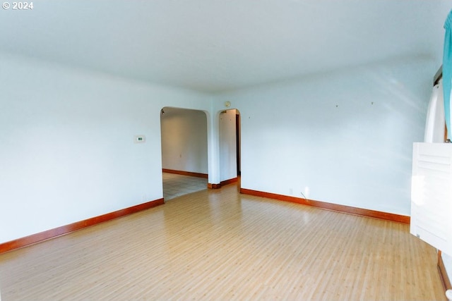 unfurnished room featuring arched walkways, light wood-type flooring, and baseboards