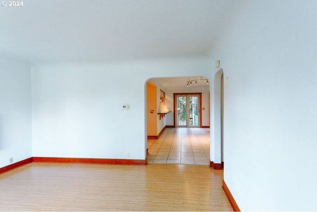 unfurnished room featuring arched walkways, baseboards, light wood-style floors, french doors, and rail lighting