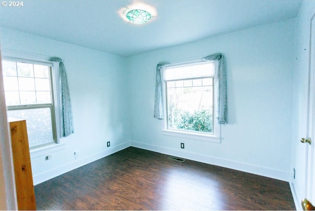 unfurnished room with dark wood-style floors, baseboards, visible vents, and a wealth of natural light