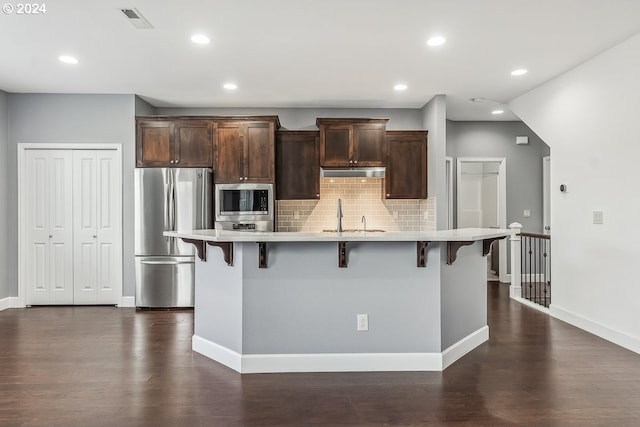 kitchen featuring a center island with sink, appliances with stainless steel finishes, a breakfast bar area, and dark hardwood / wood-style flooring