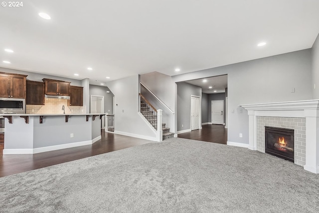 unfurnished living room featuring sink, dark wood-type flooring, and a fireplace