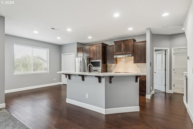 kitchen with dark wood-type flooring, stainless steel appliances, an island with sink, and a kitchen breakfast bar