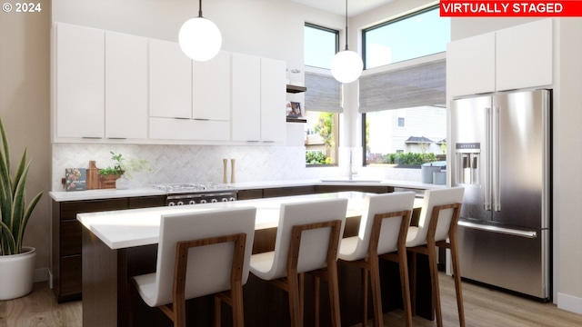 kitchen with light wood-type flooring, high quality fridge, sink, a kitchen island, and hanging light fixtures