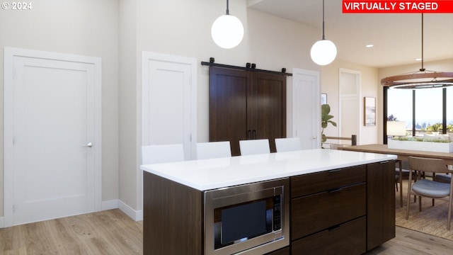 kitchen with dark brown cabinets, a barn door, decorative light fixtures, light hardwood / wood-style flooring, and stainless steel microwave