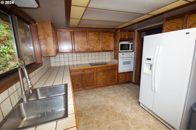 kitchen featuring tile countertops, white appliances, sink, a drop ceiling, and tasteful backsplash