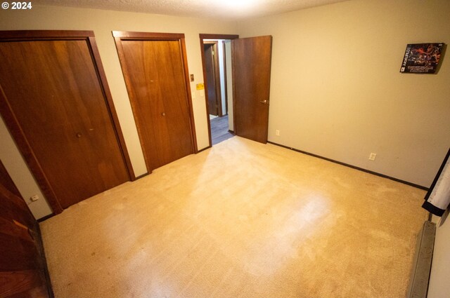 unfurnished bedroom with light carpet and two closets